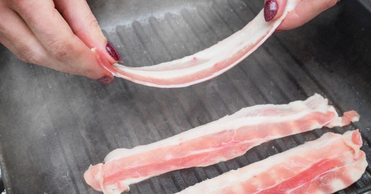 womans hands cooking bacon on a griddle
